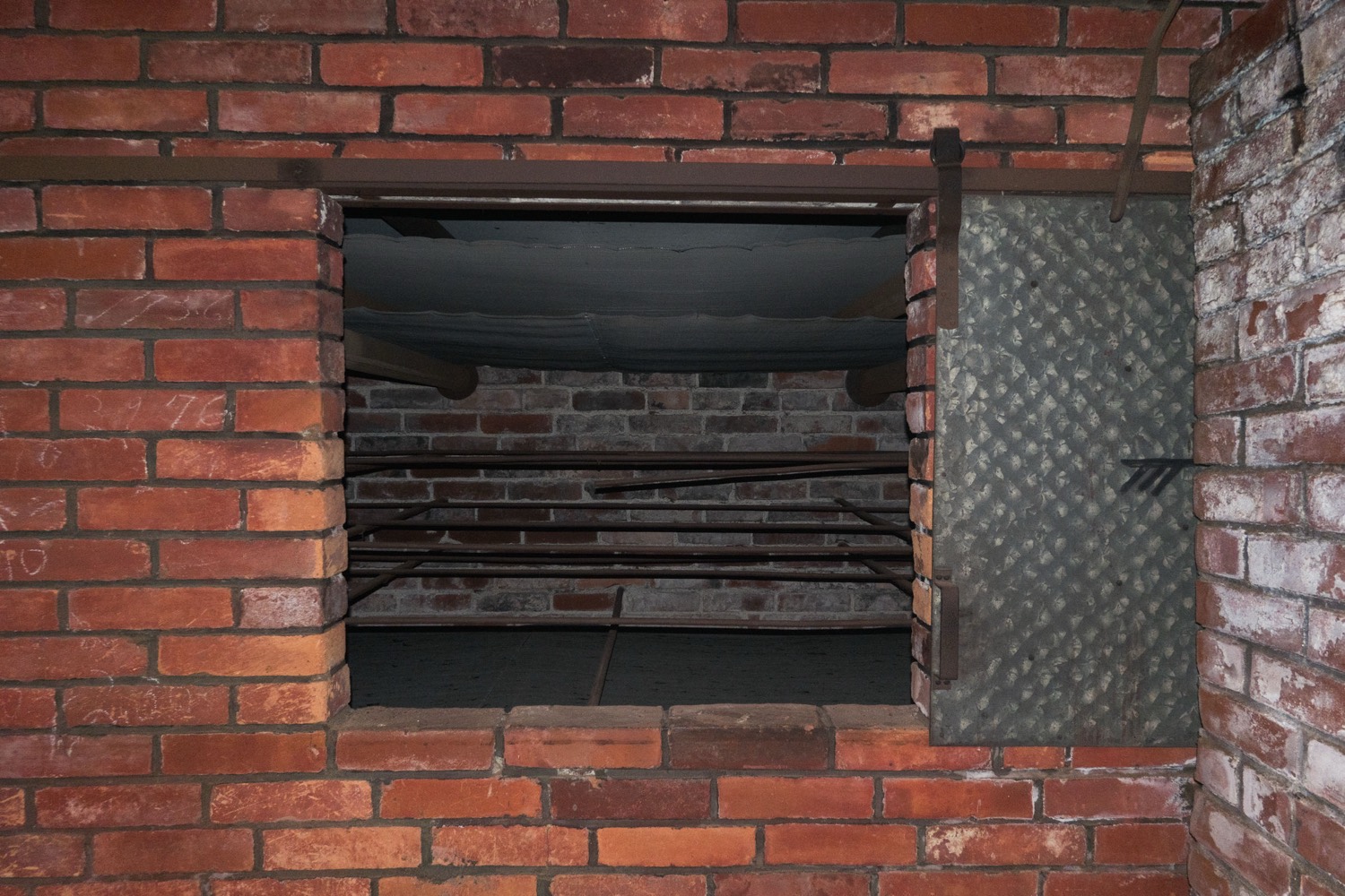 The open mouth of a red-brick tencha oven, with iron drying rails and a hanging cloth inside